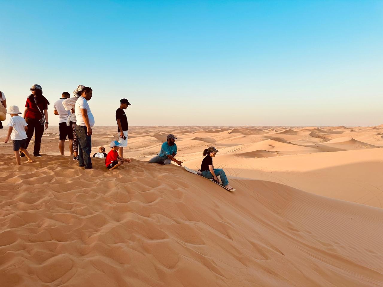 Group sandboarding and relaxing on the golden dunes in Dubai